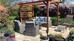 Patio in garden with chairs, sofa and table surrounded by flowers