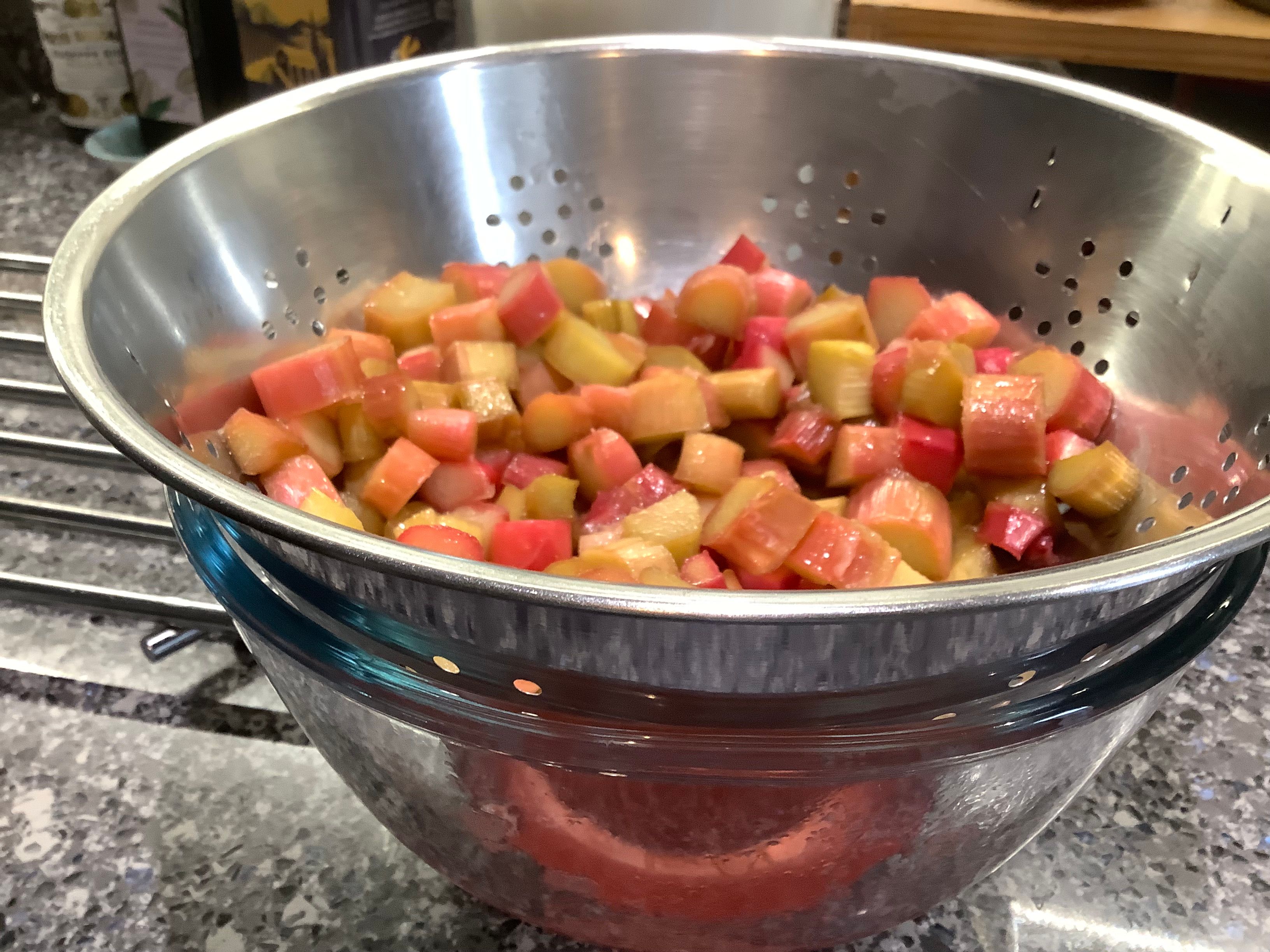 Baked rhubarb in a strainer over a glass bowl in which rhubarb juice has been collected