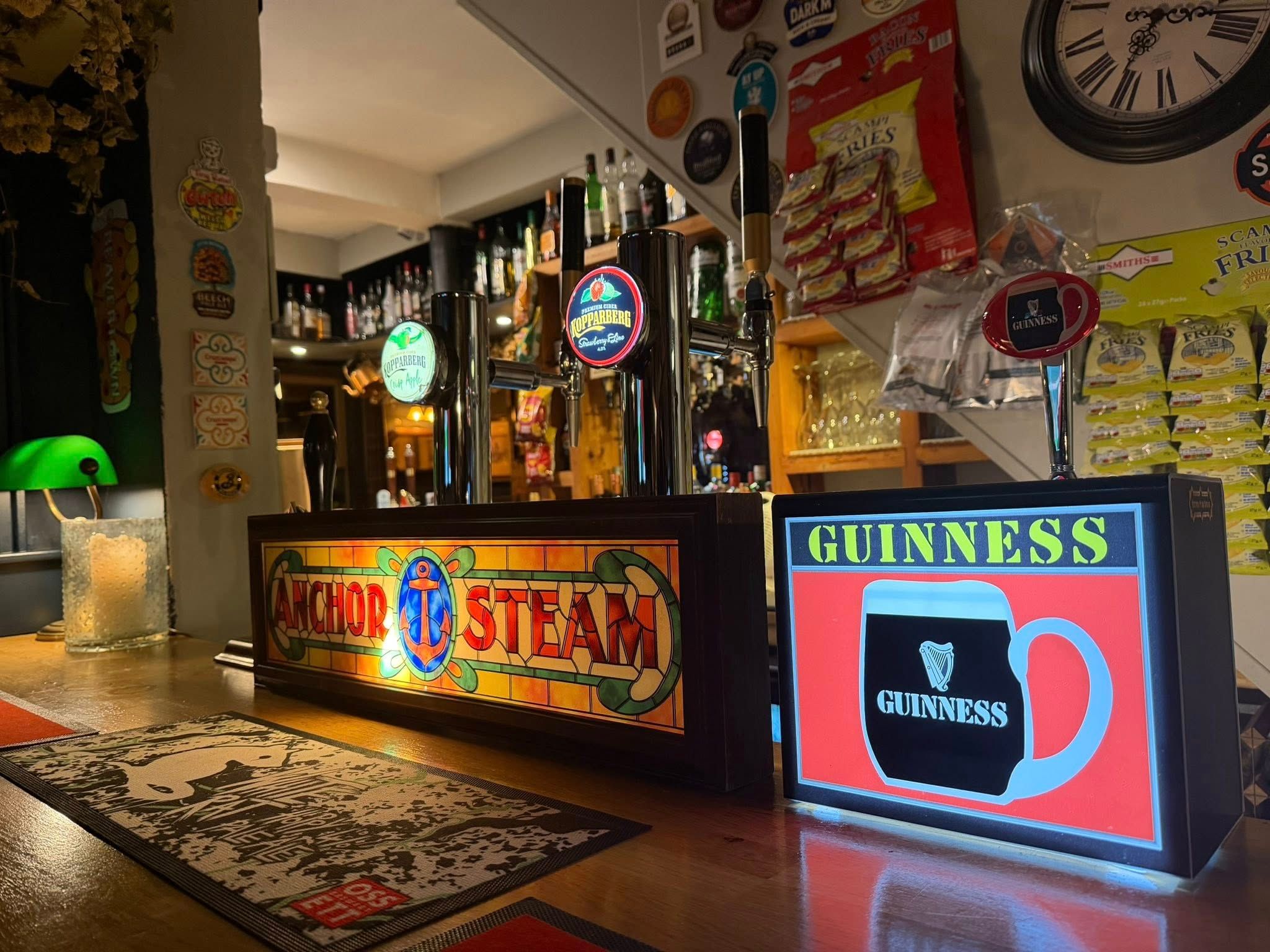 Bar counter with illuminated Anchor Steam and Guinness signs, tap handles, and snacks on display