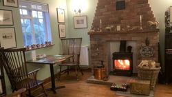 Cozy room with a wood-burning stove, brick fireplace, wooden chairs, and framed pictures on the wall.