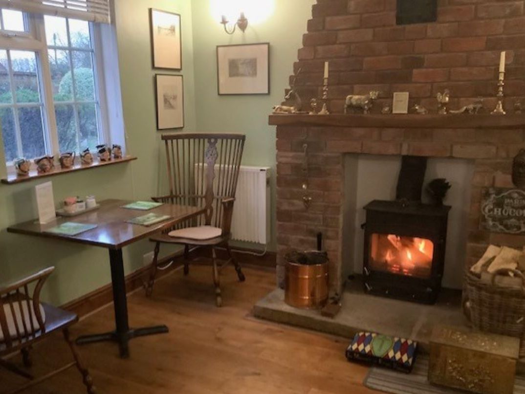Cozy dining room with wooden chairs, a table set for two, and a brick fireplace with a fire burning inside.