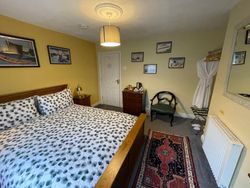 Kingsize bed in Bedroom 3 with bedside table and lamp, chest of drawers with hospitality tray, chair, and entrance door