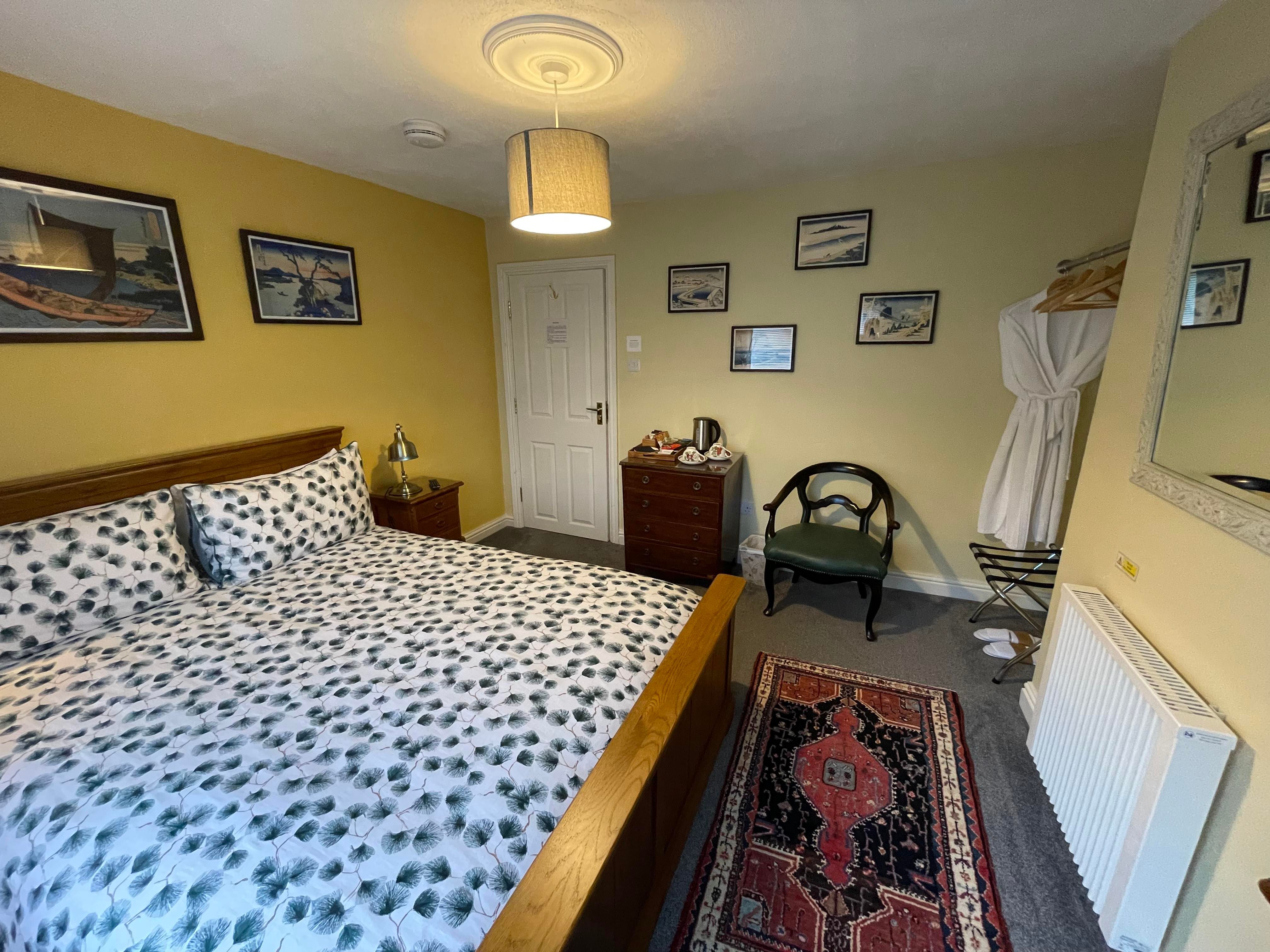 Kingsize bed in Bedroom 3 with bedside table and lamp, chest of drawers with hospitality tray, chair, and entrance door