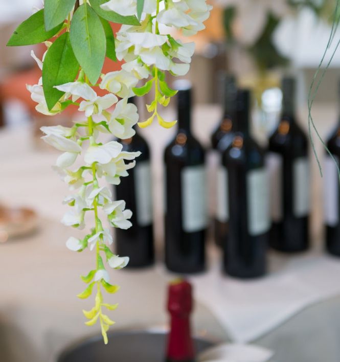 Close-up of white wisteria flowers hanging with wine bottles and a champagne bottle in a bucket in the background.