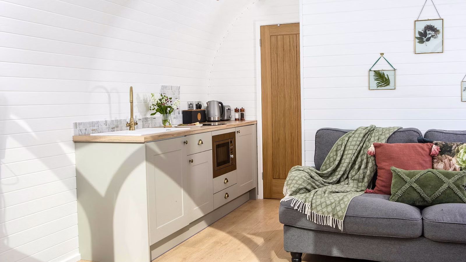 Grey sofa with pink and green cushions, kitchen in Heather Pod