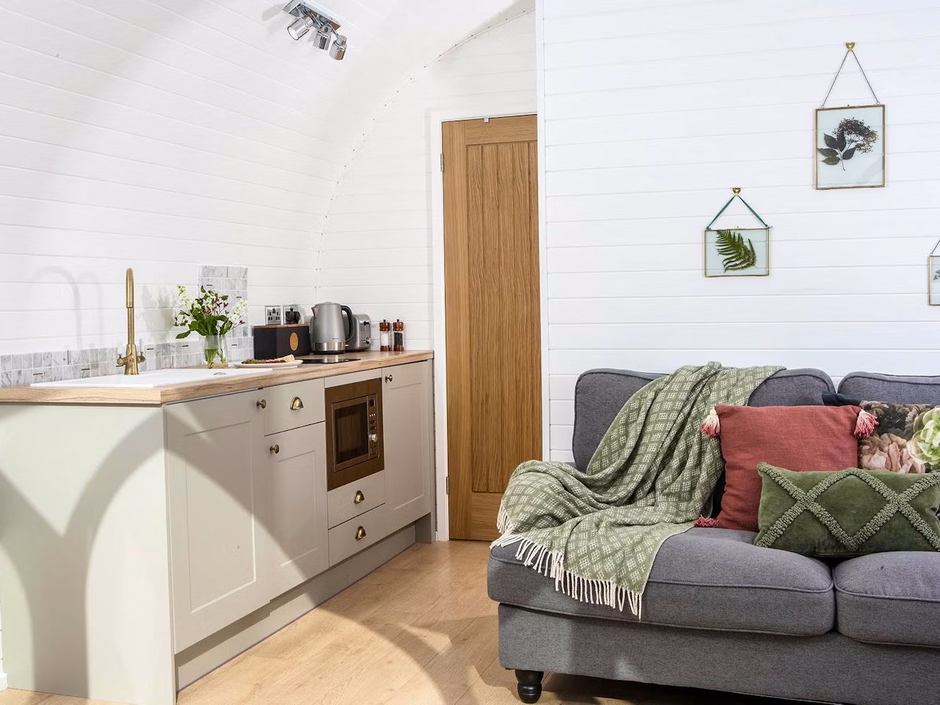 Grey sofa with pink and green cushions, kitchen in Heather Pod