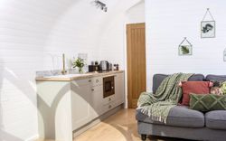 Grey sofa with pink and green cushions, kitchen in Heather Pod