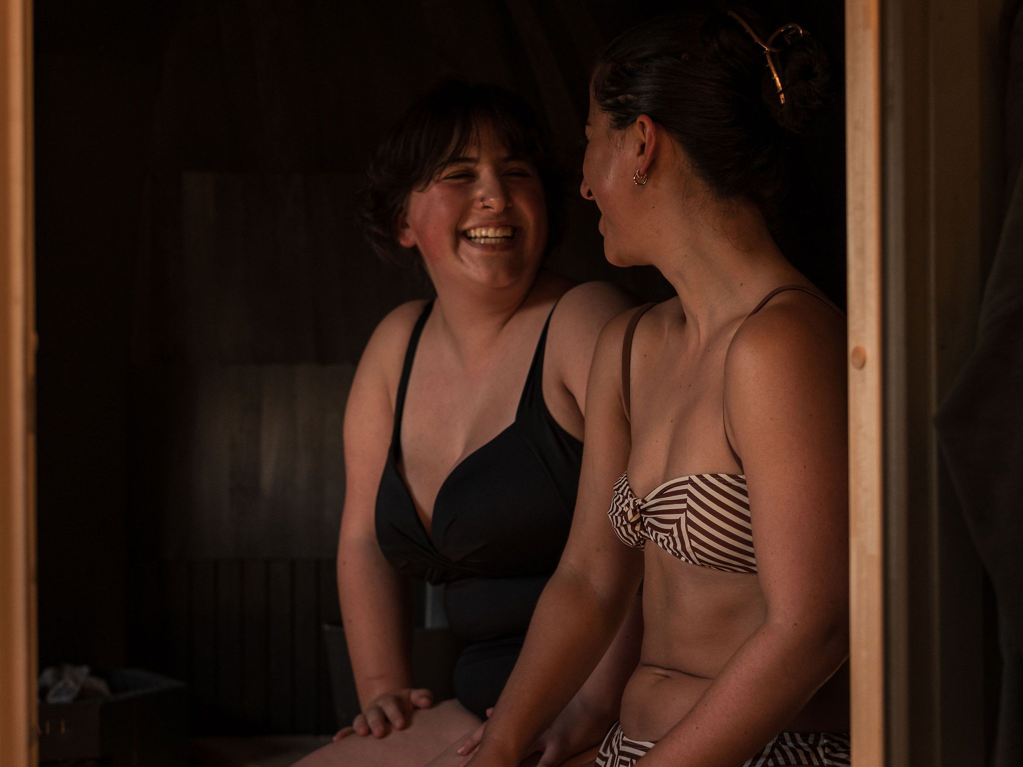 Two women in swimsuits sitting and smiling together inside an Iglusauna.
