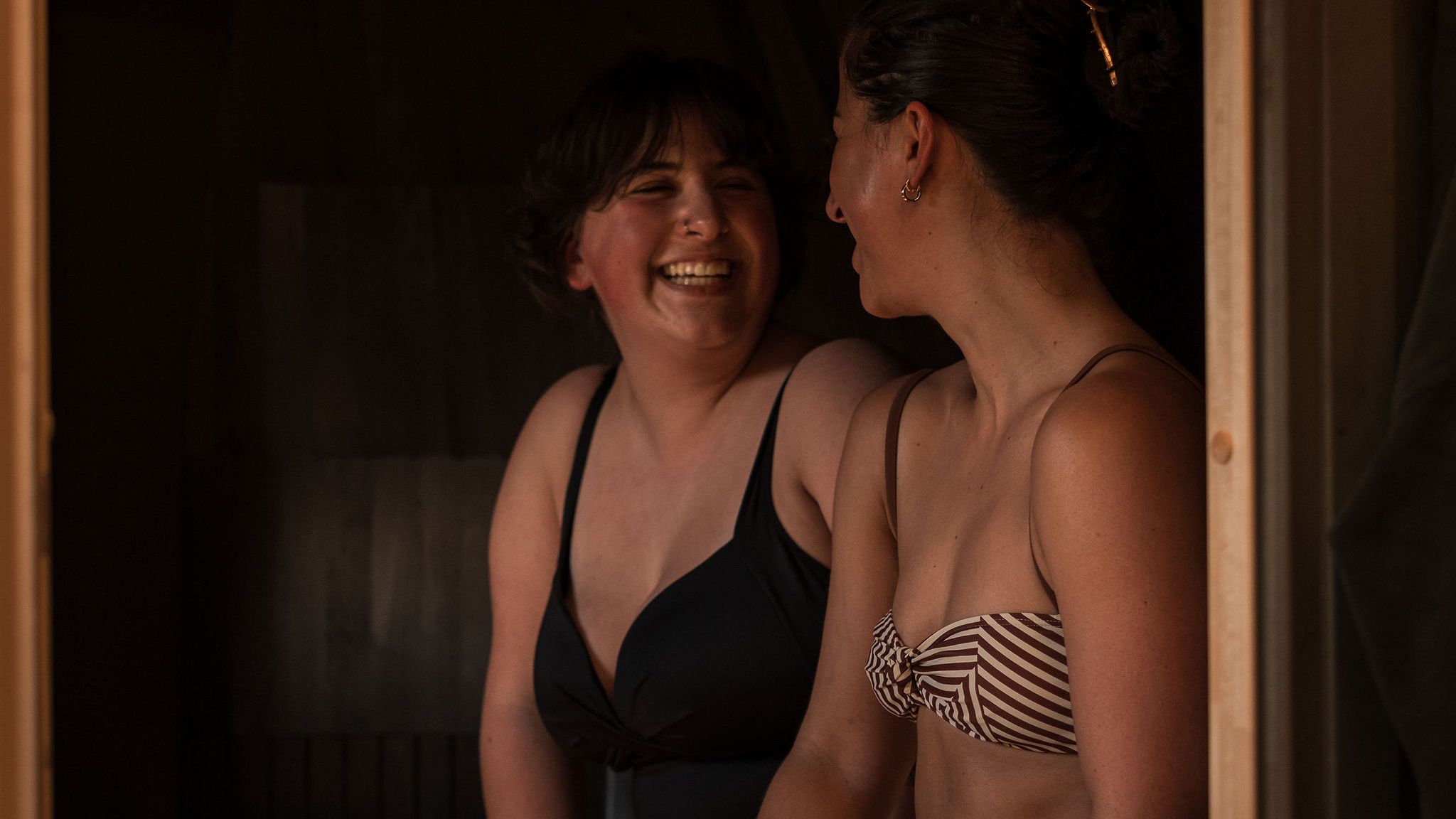 Two women in swimsuits sitting and smiling together inside an Iglusauna.
