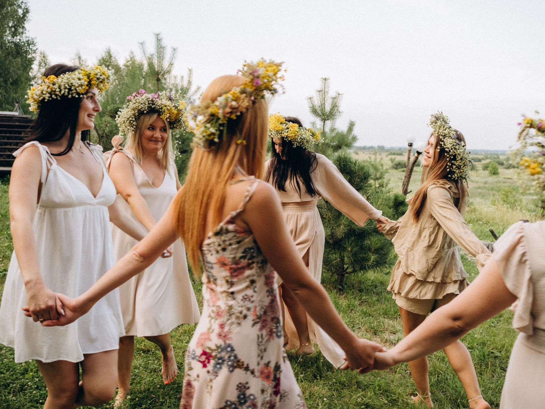 Women wearing flower crowns holding hands in a circle outdoors