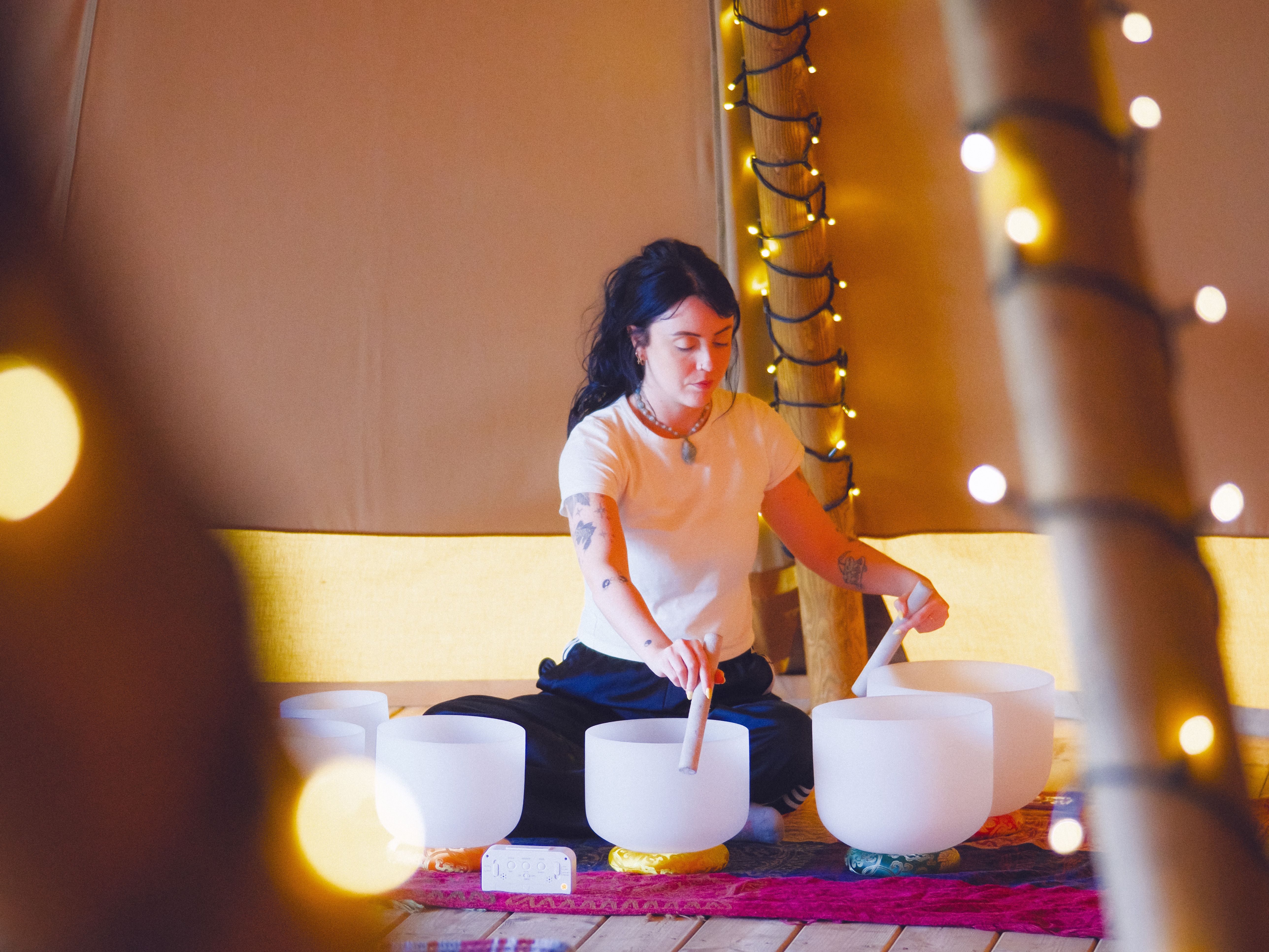 Person playing crystal singing bowls in a softly lit room with fairy lights