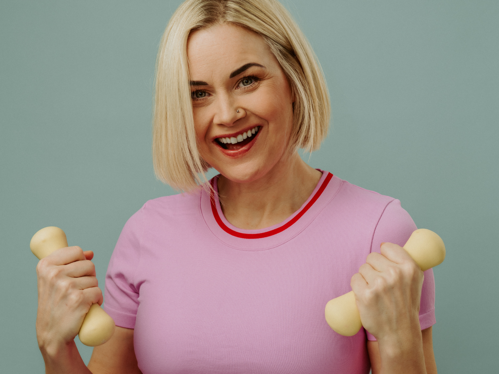 Smiling woman holding two dumbbells against a plain background