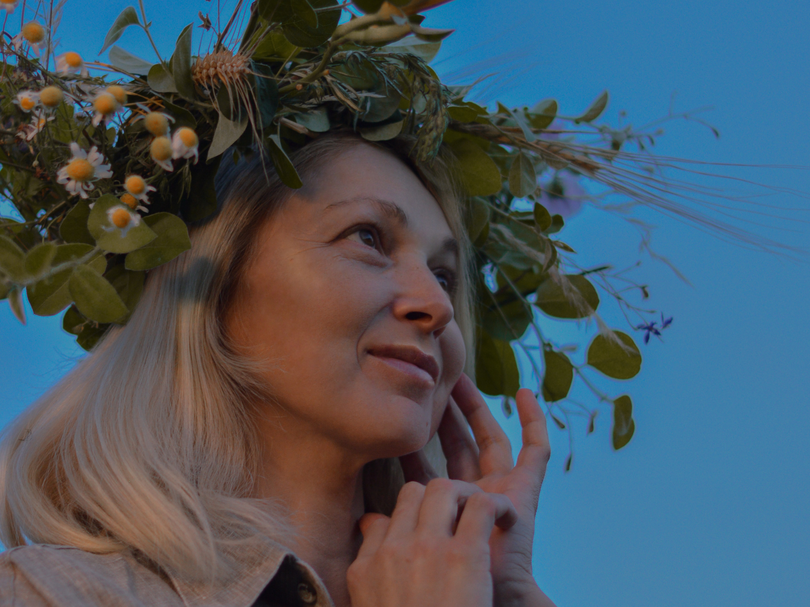 Woman wearing a floral and leafy crown, looking up against a clear blue sky