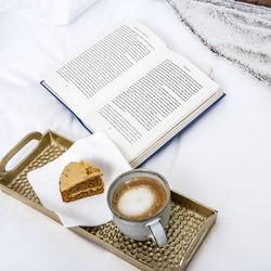 Coffee and cake on tray with book on bed