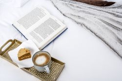 Coffee and cake on tray with book on bed