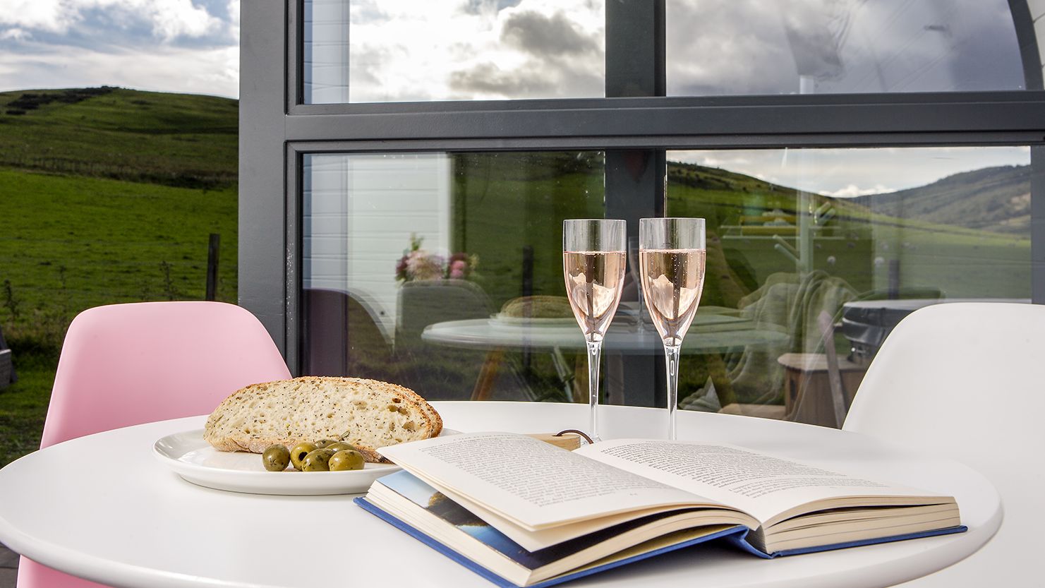 Prosecco and book on table with view outside glamping pod