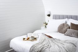 Tray of tea and cake with a book on bed with grey cushions