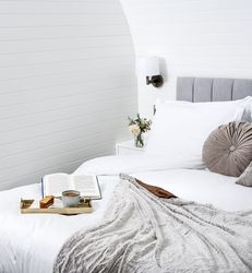 Tray of tea and cake with a book on bed with grey cushions