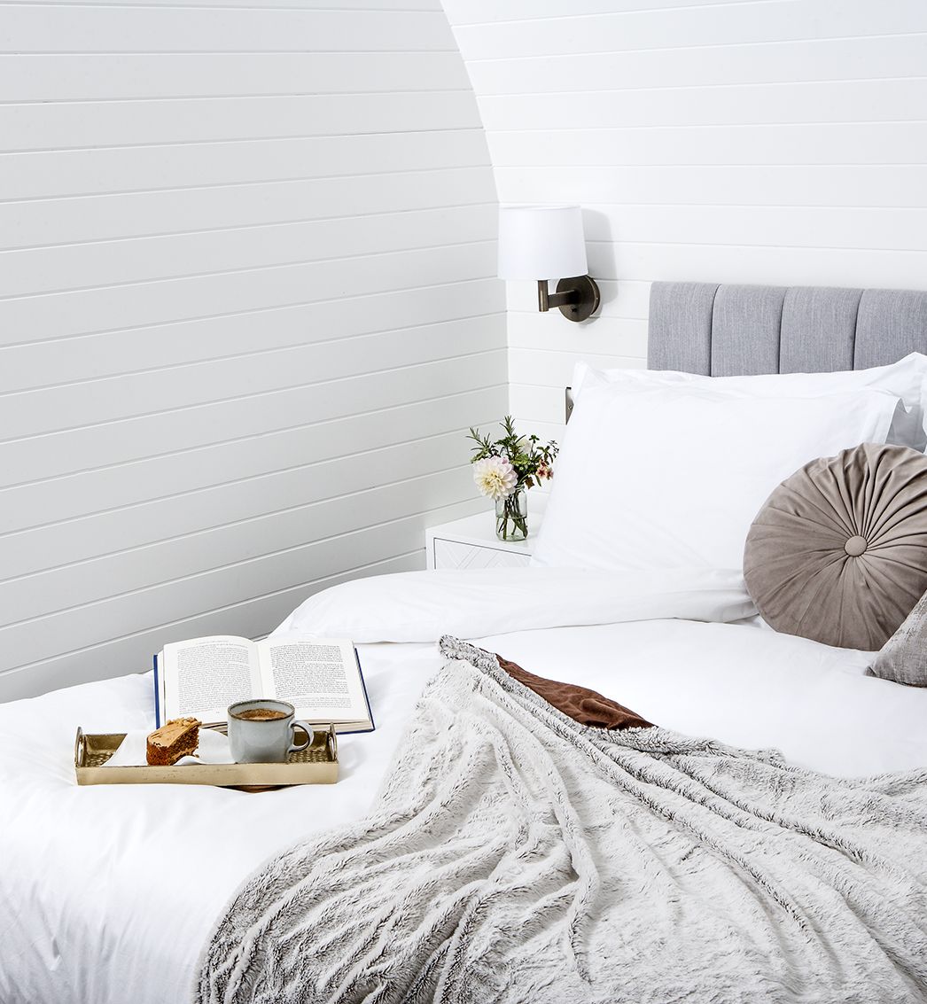 Tray of tea and cake with a book on bed with grey cushions