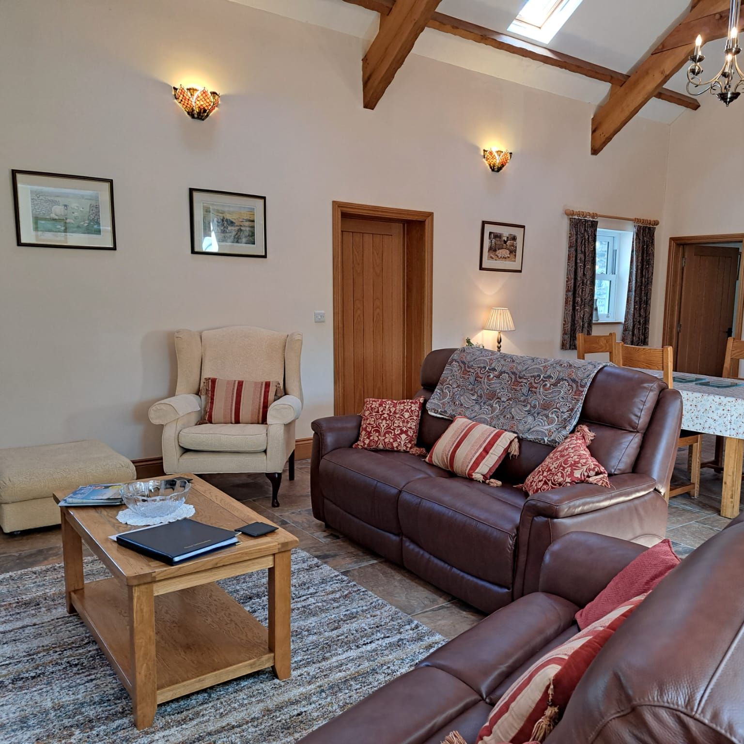 Cozy living room with leather sofas, a beige armchair, wooden coffee table, dining area, and wooden staircase leading upstairs.