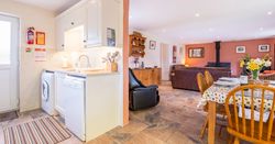 Cothi Cottage open plan living area, large brown leather sofas, with washing machine and fridge in the kitchen