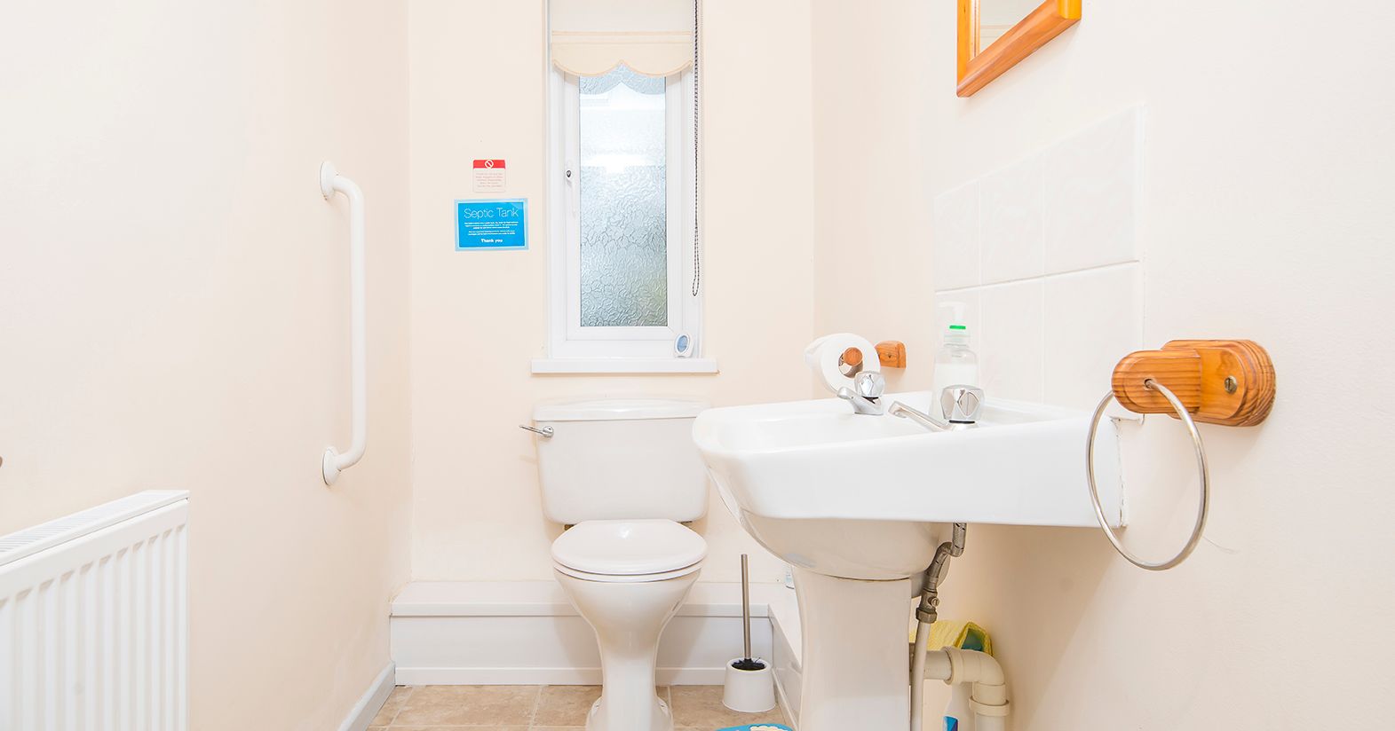 A compact bathroom with a white toilet and pedestal sink. A frosted window lets in natural light, and a grab rail is mounted on the wall for accessibility.