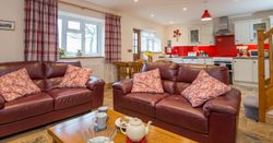 A cosy open-plan living area in Teifi Cottage with brown leather sofas, a wooden coffee table set for tea, and a modern kitchen with red accents in the background.