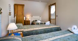 A cosy bedroom in Teifi Cottage with three single beds dressed in green and cream bedding. Warm lighting, wooden furniture, and neatly folded towels create a welcoming space.