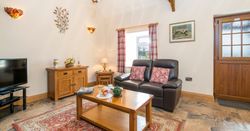 A cozy living room with a leather sofa, wooden furniture, and a red patterned rug. A coffee table is set for tea, with a TV, wall décor, and a wooden door adding charm.
