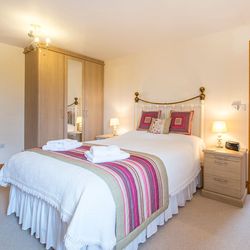 A cozy bedroom with a brass bed frame, white bedding, and a striped throw in shades of pink and green. A wardrobe with mirrors stands beside bedside tables with lamps.