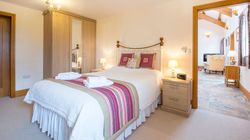 A cozy bedroom with a brass bed frame, white bedding, and a striped throw in shades of pink and green. A wardrobe with mirrors stands beside bedside tables with lamps.