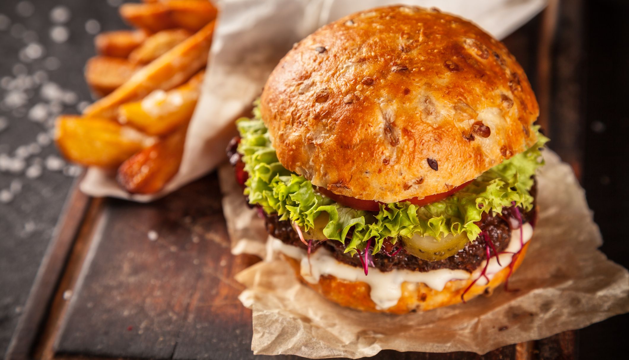 beef burger on a wooden board with a seeded roll and thick cut chips