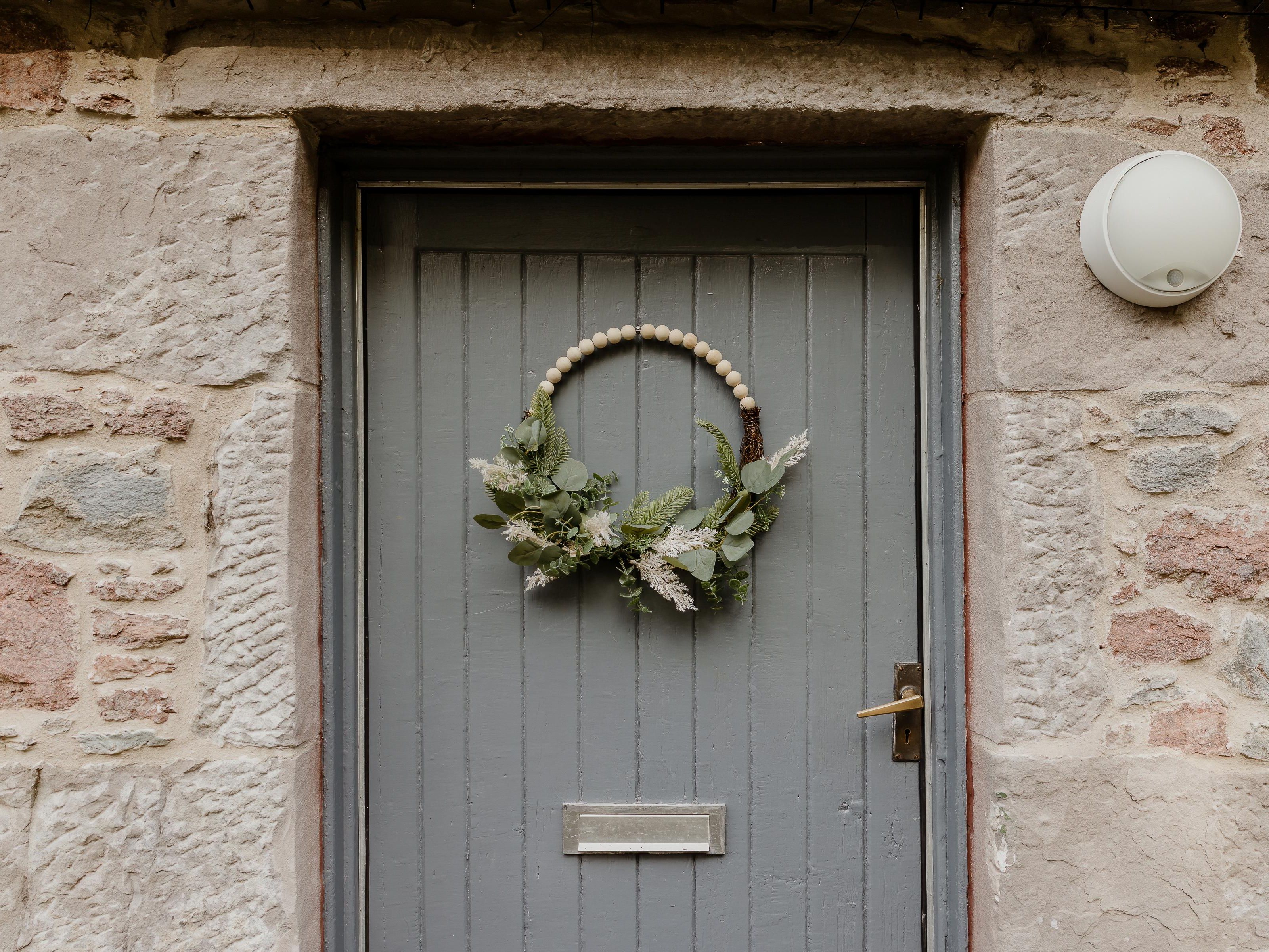 Grey wooden door in a stone wall with a greenery wreath and a round wall light