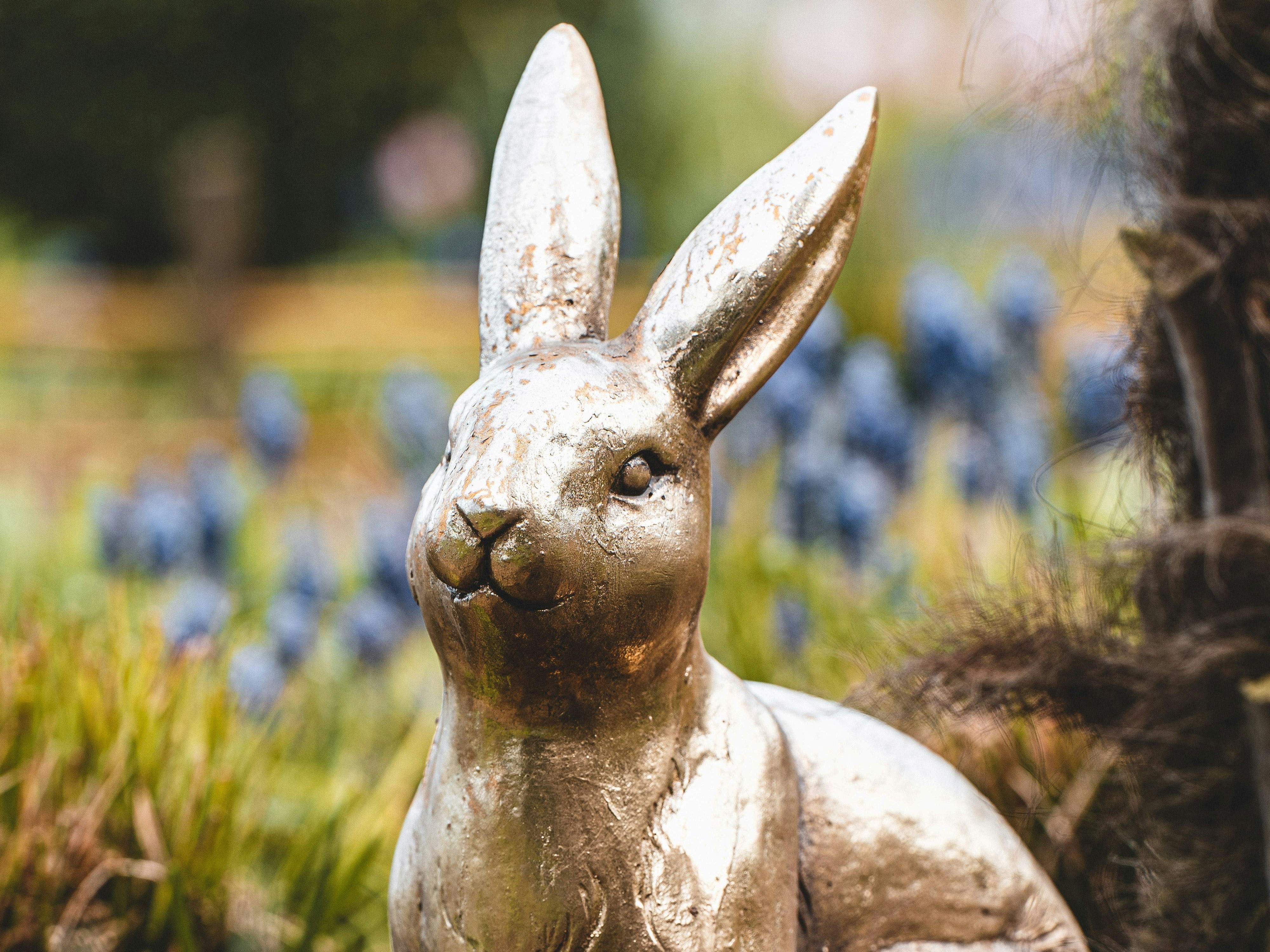Bronze rabbit statue in a garden among blue flowers