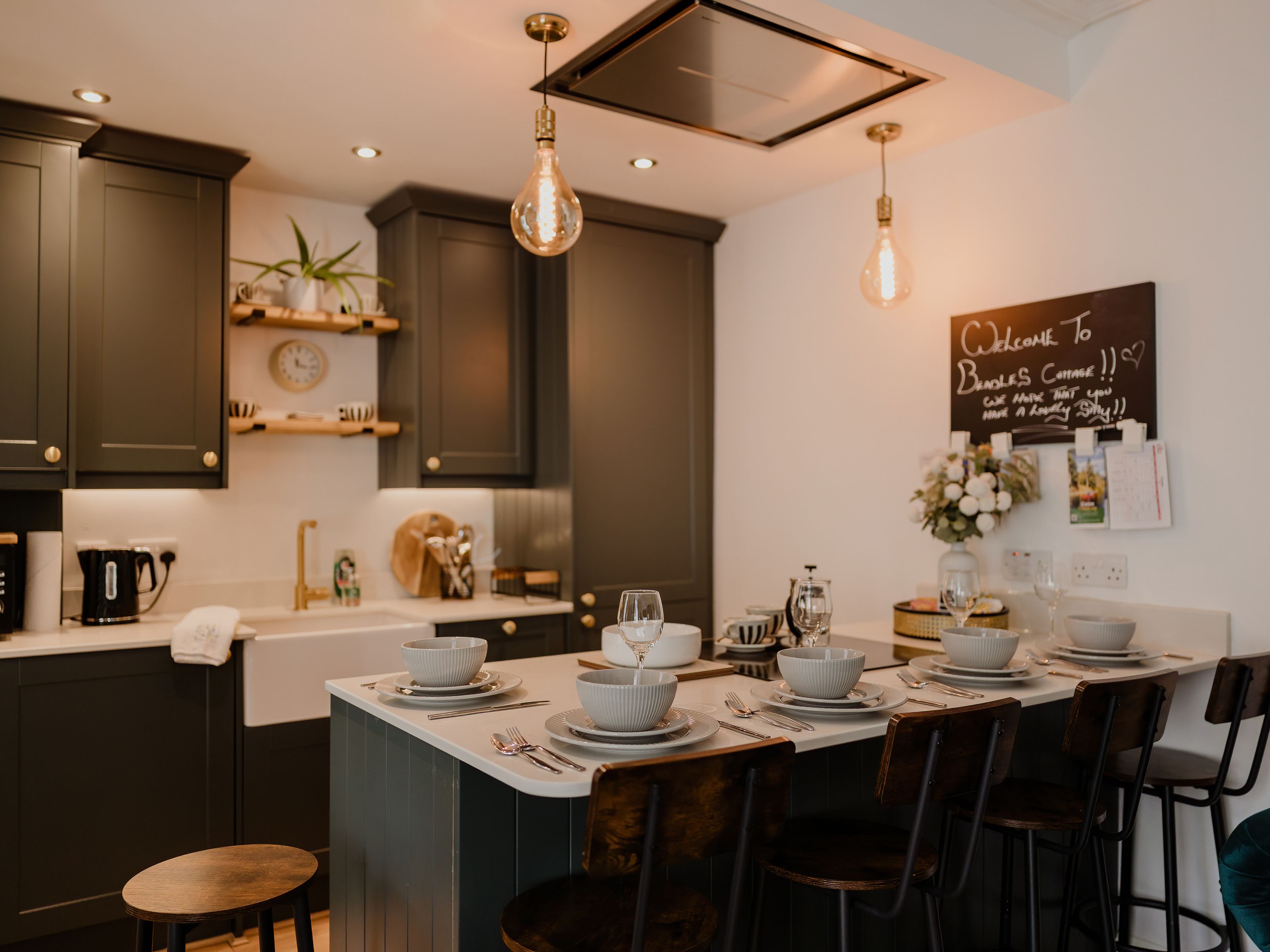 Modern kitchen with dark grey cabinets, pendant lights and a breakfast bar set with bowls and glasses