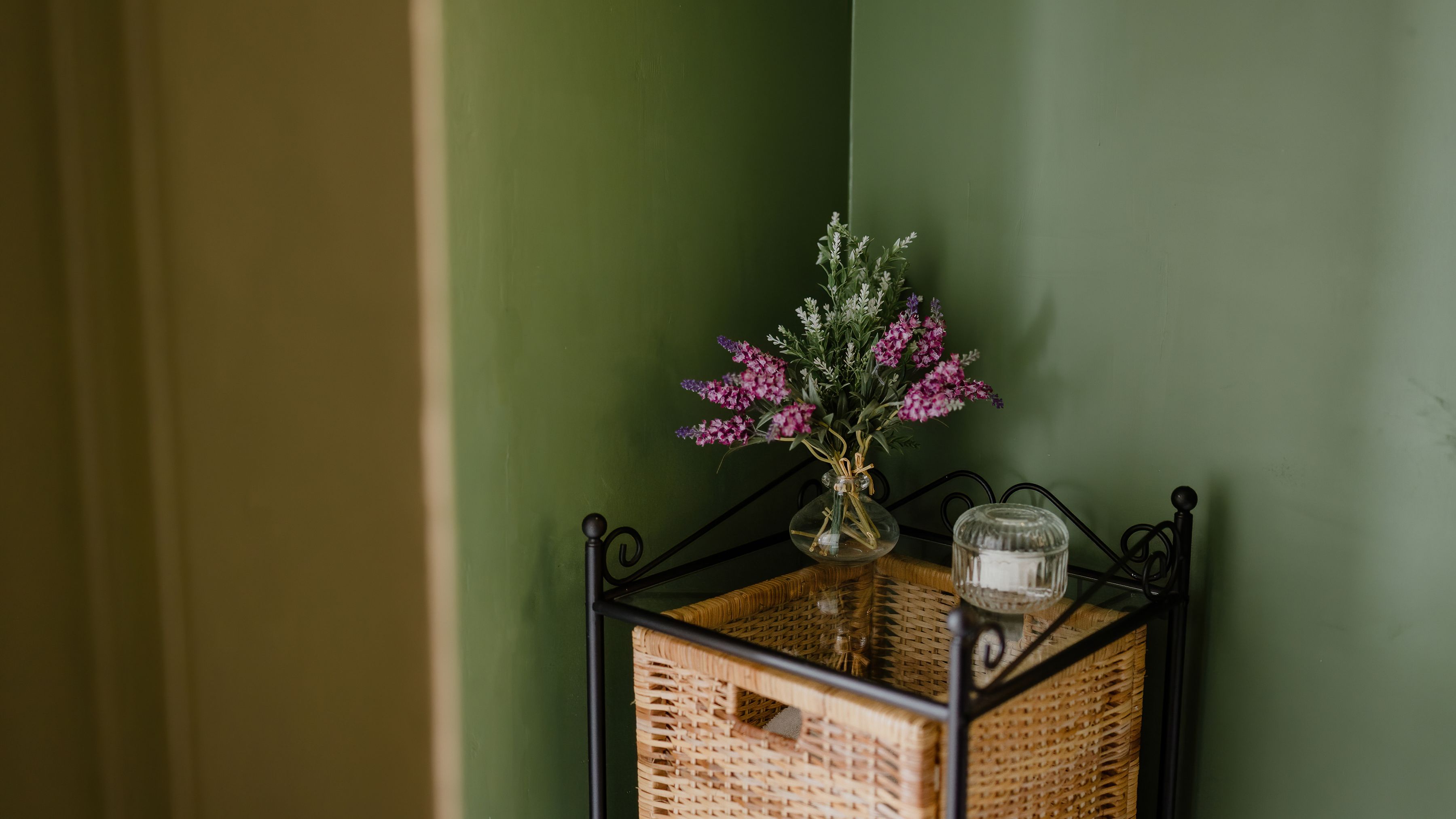 Small side table with a glass vase of purple flowers against a green wall