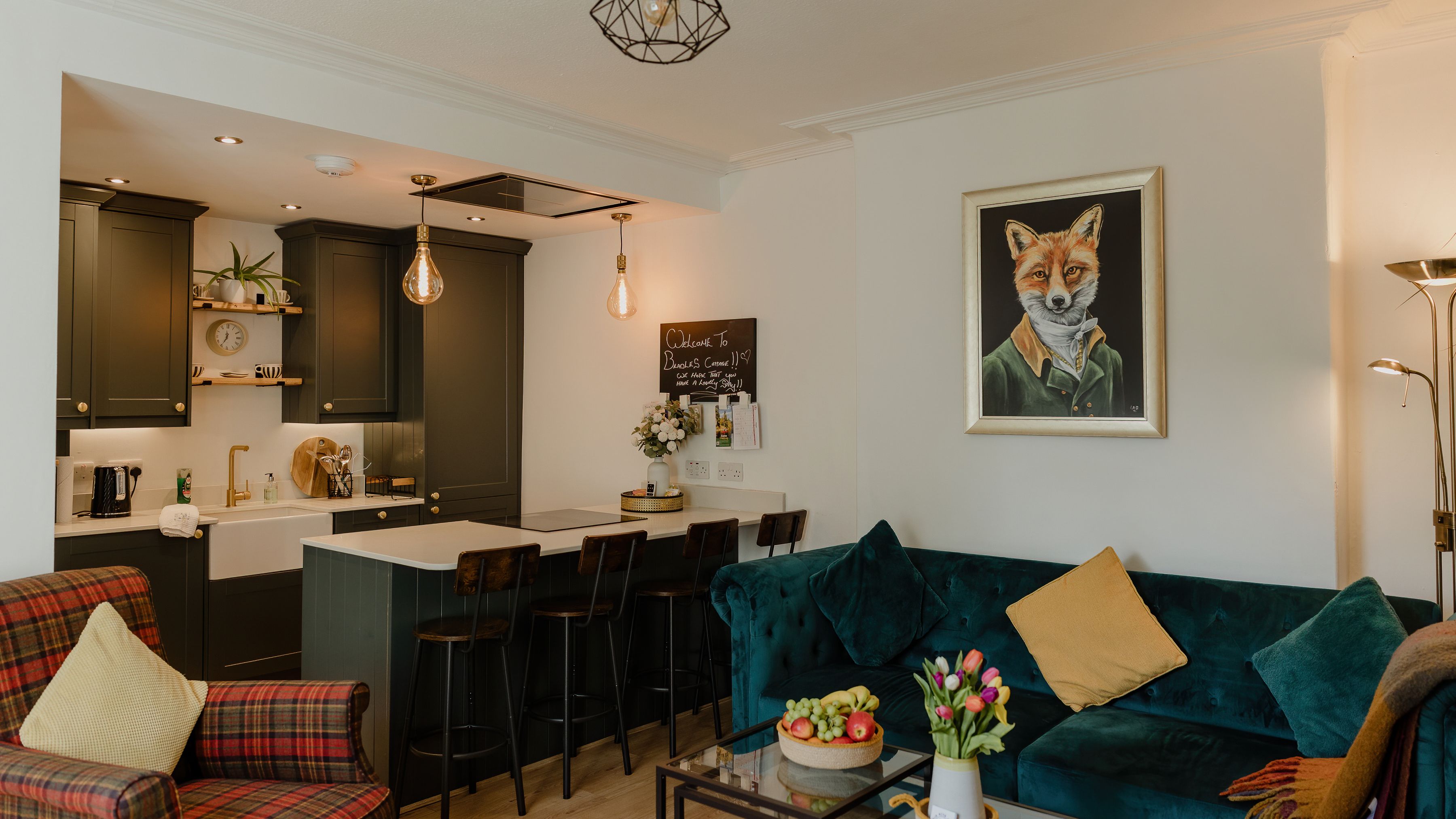 Modern open-plan kitchen and living room with dark cabinets, breakfast bar stools, teal sofa and fox artwork