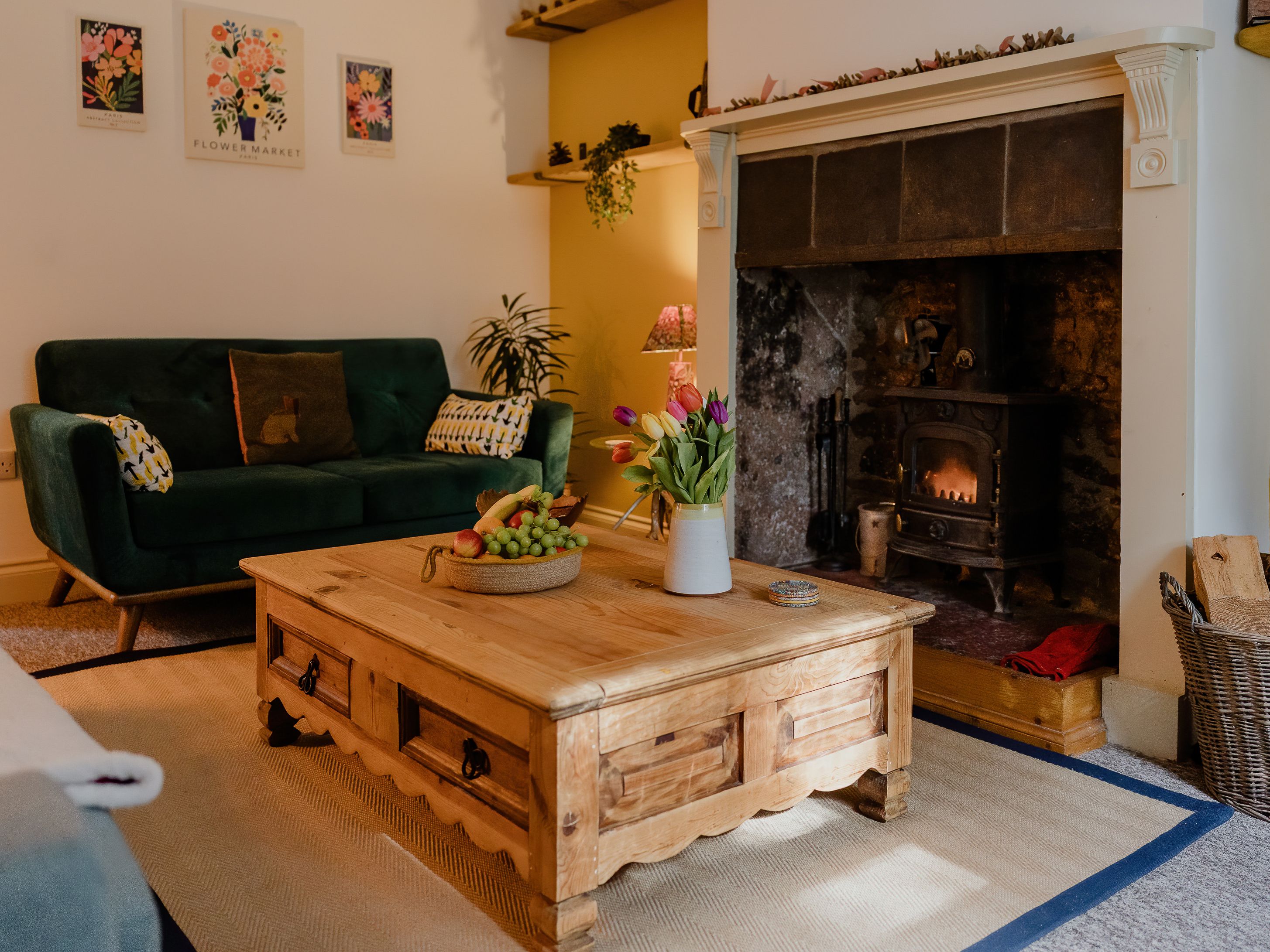 Cosy living room with green sofa, wooden coffee table and lit wood-burning stove