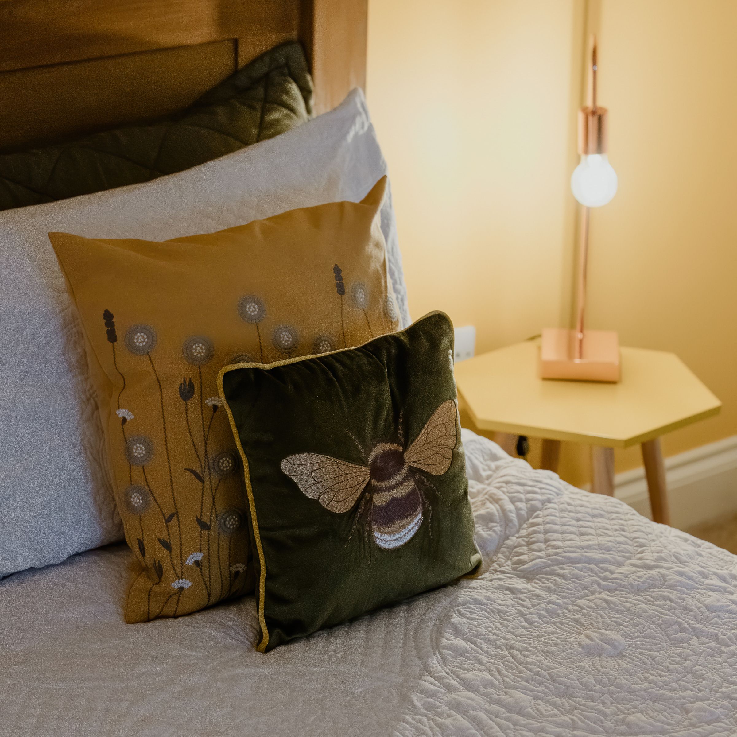Cosy bed with patterned cushions beside a bedside table and lit lamp