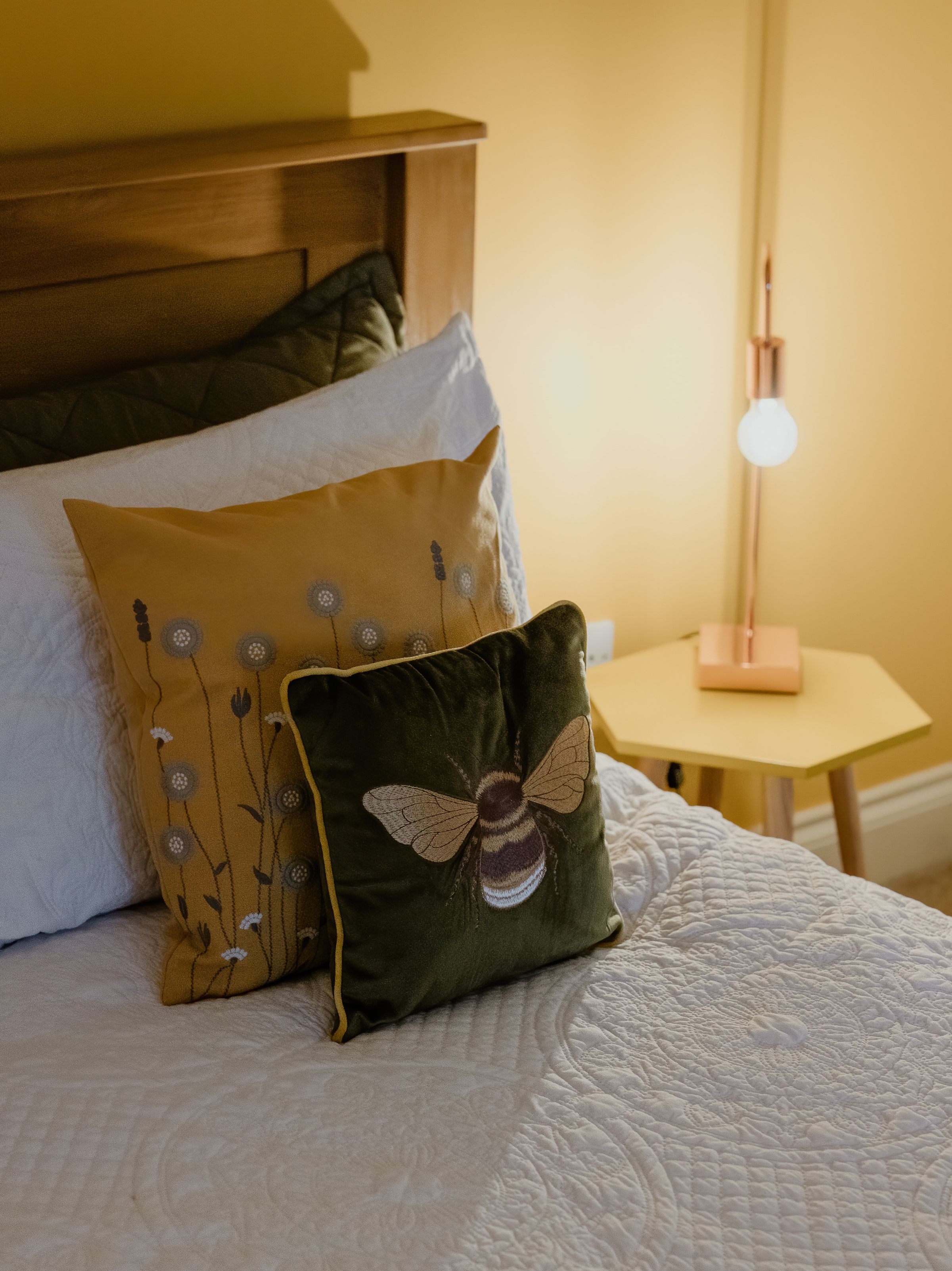 Cosy bed with patterned cushions beside a bedside table and lit lamp