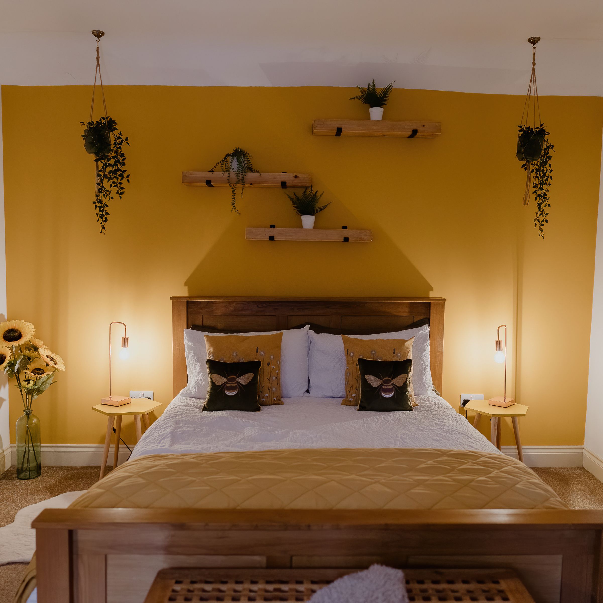 Cosy bedroom with mustard feature wall, wooden bed, bedside lamps and hanging plants