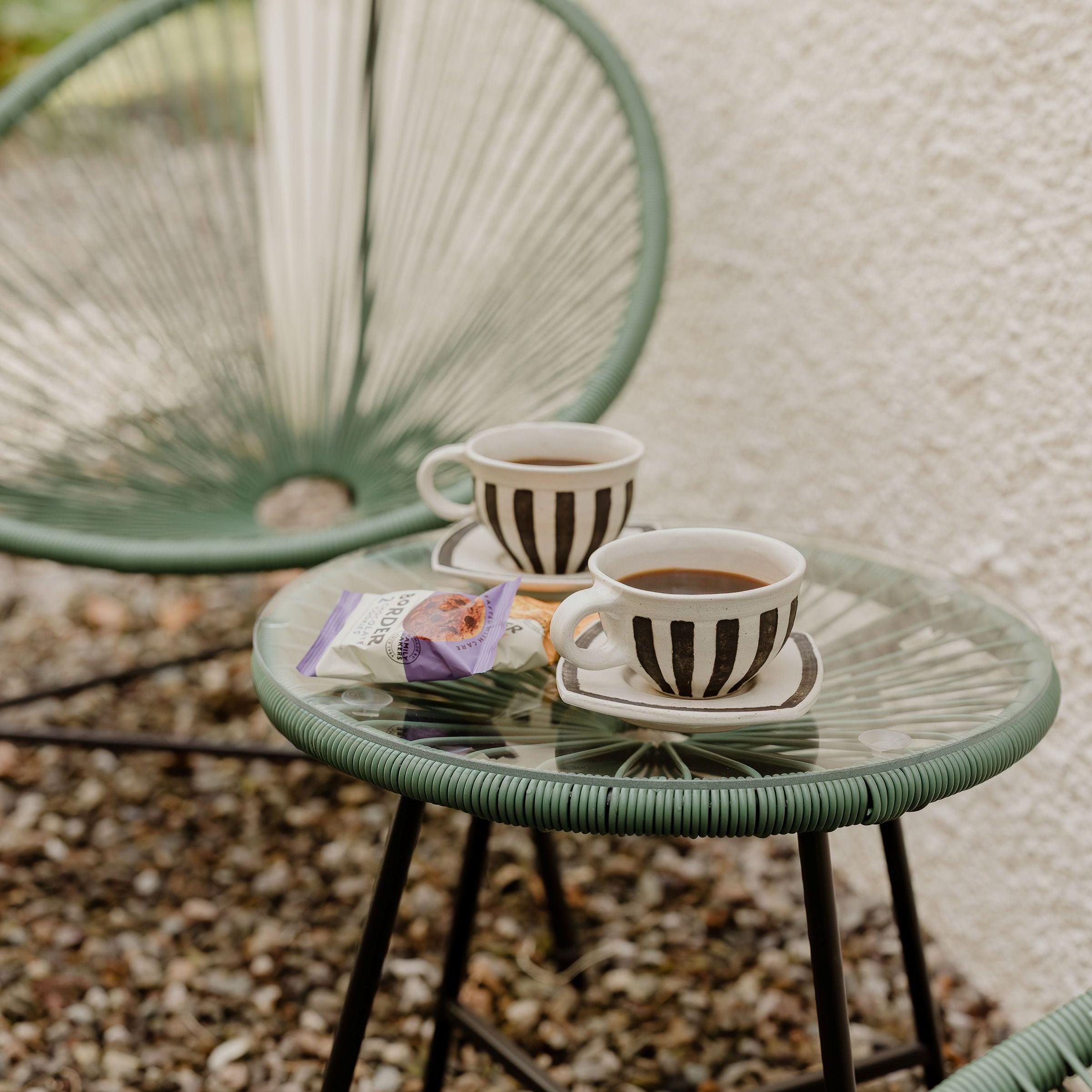 Two striped coffee cups on a green wire café table outdoors
