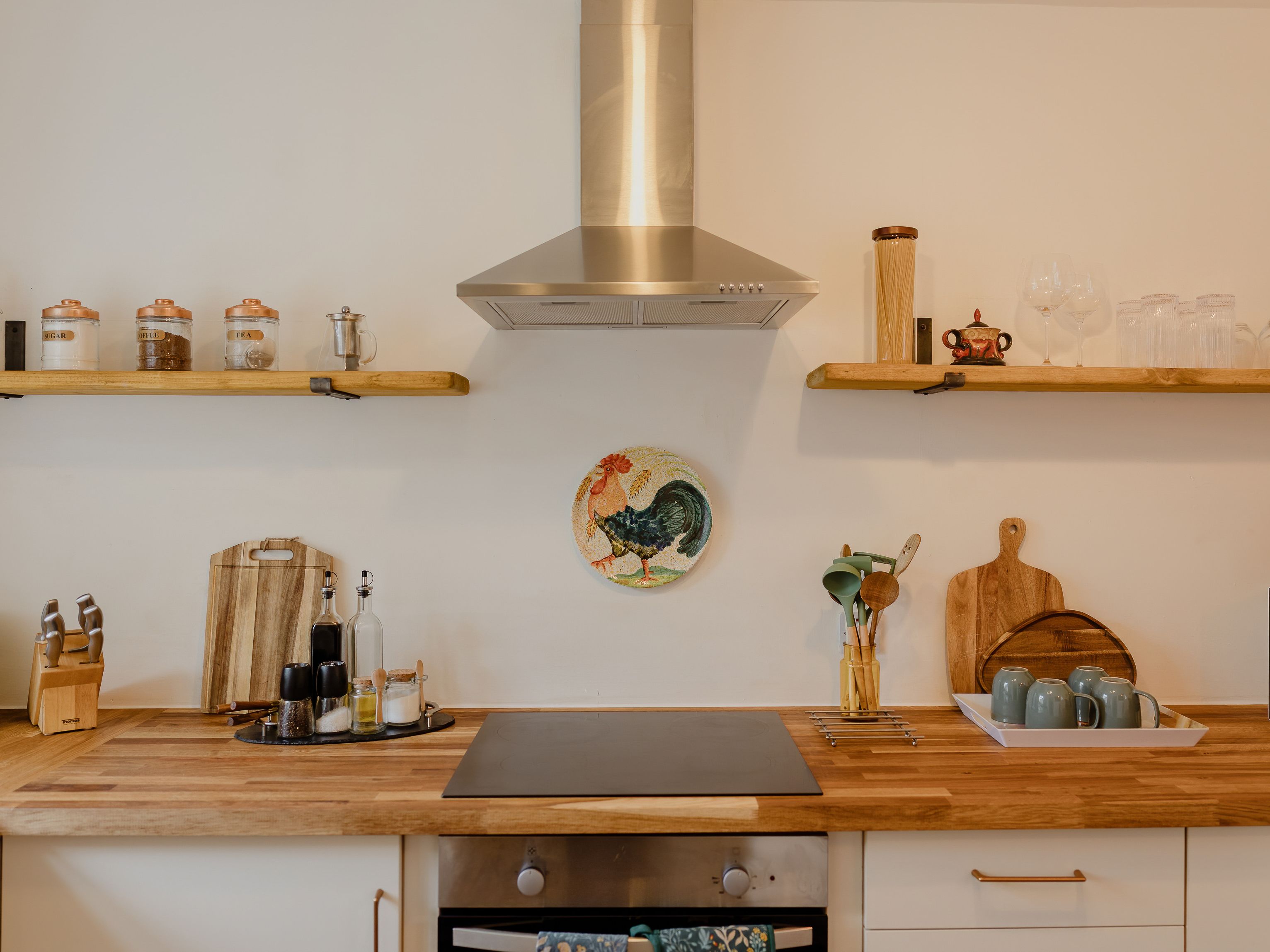 Neat kitchen worktop with stainless-steel cooker hood, wooden shelves, and jars labelled sugar, coffee and tea