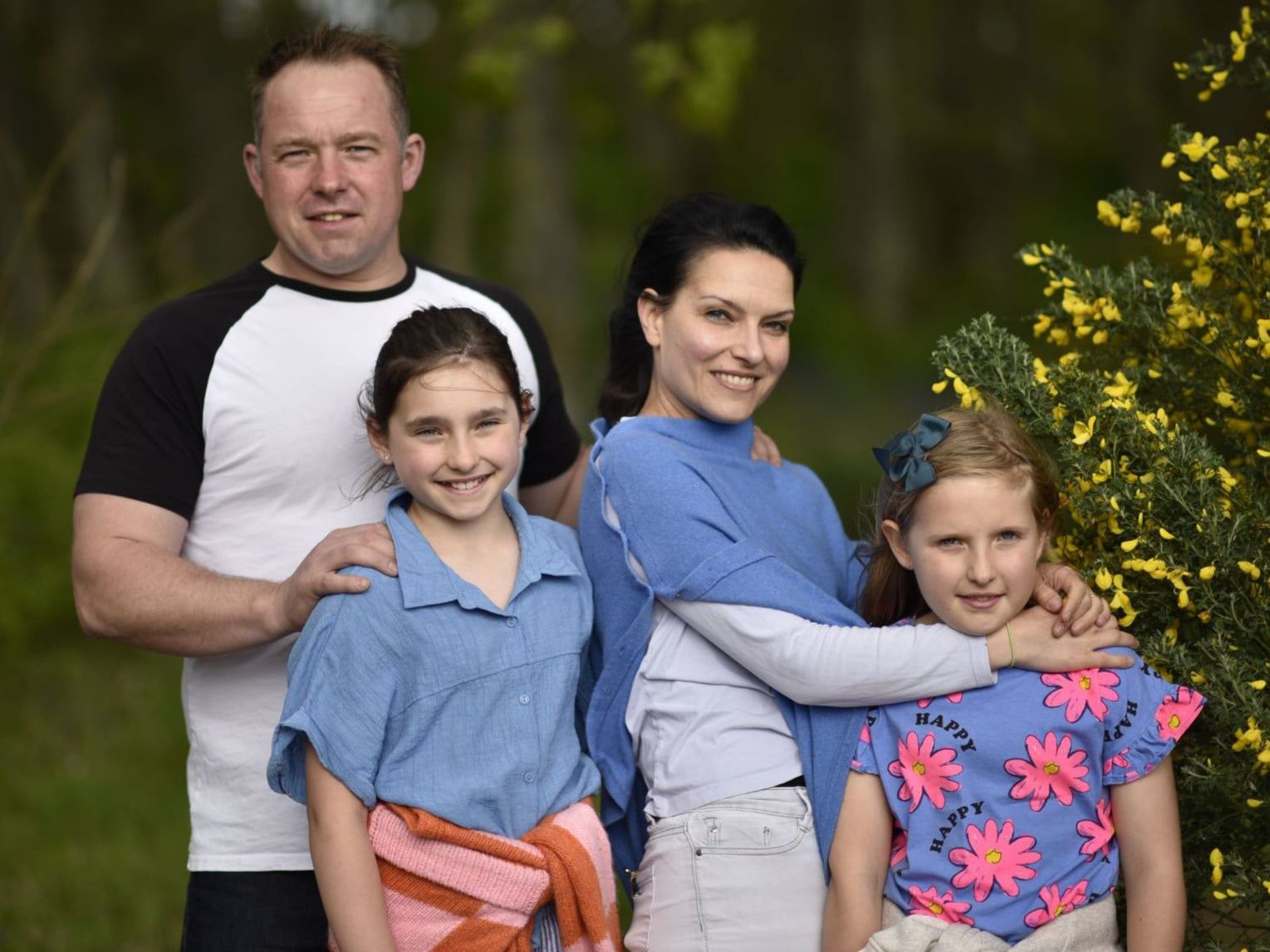 Family of four posing outdoors beside a yellow flowering bush