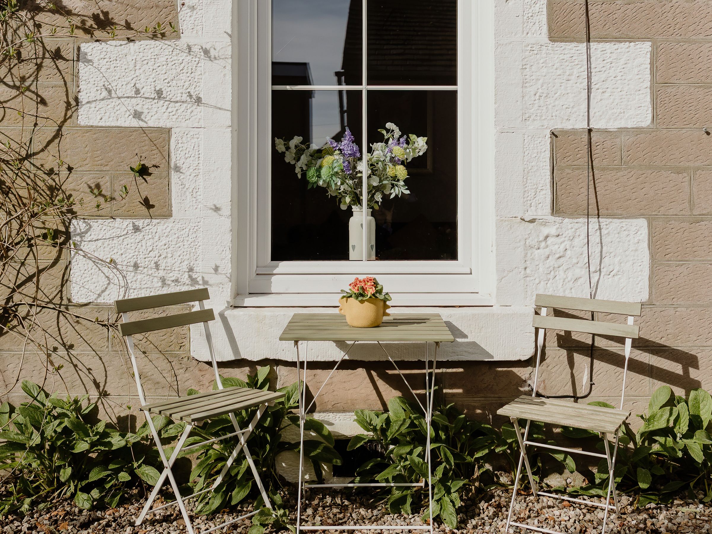 Small patio set with two chairs and a table in front of a cottage window