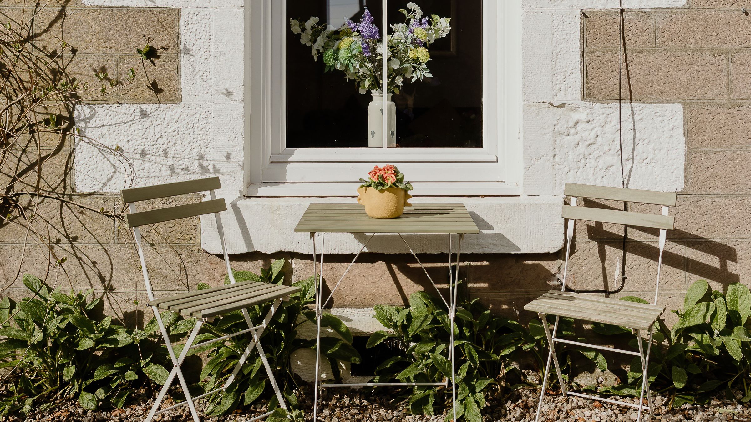 Small patio set with two chairs and a table in front of a cottage window