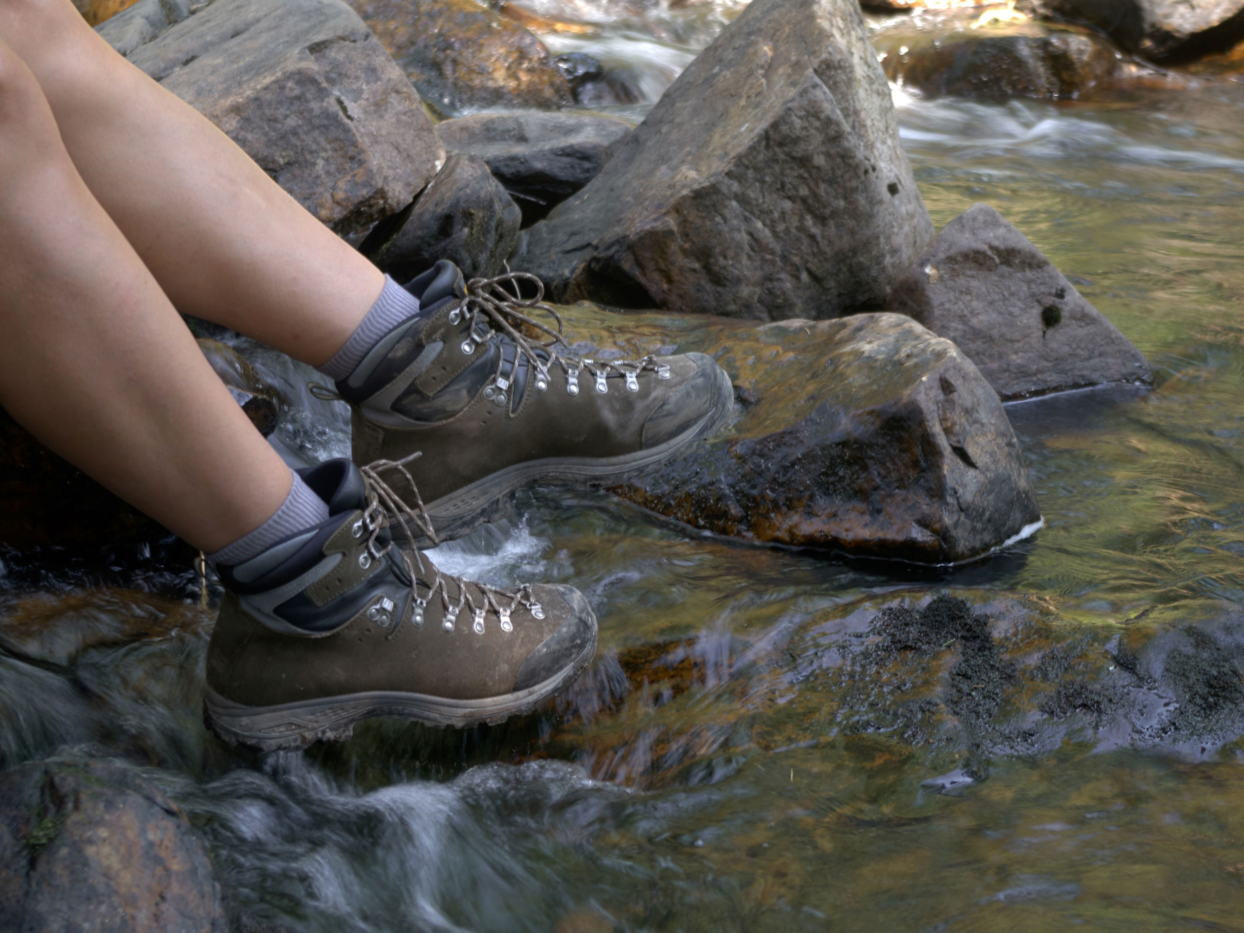Hiker’s legs in walking boots resting on rocks in a shallow stream