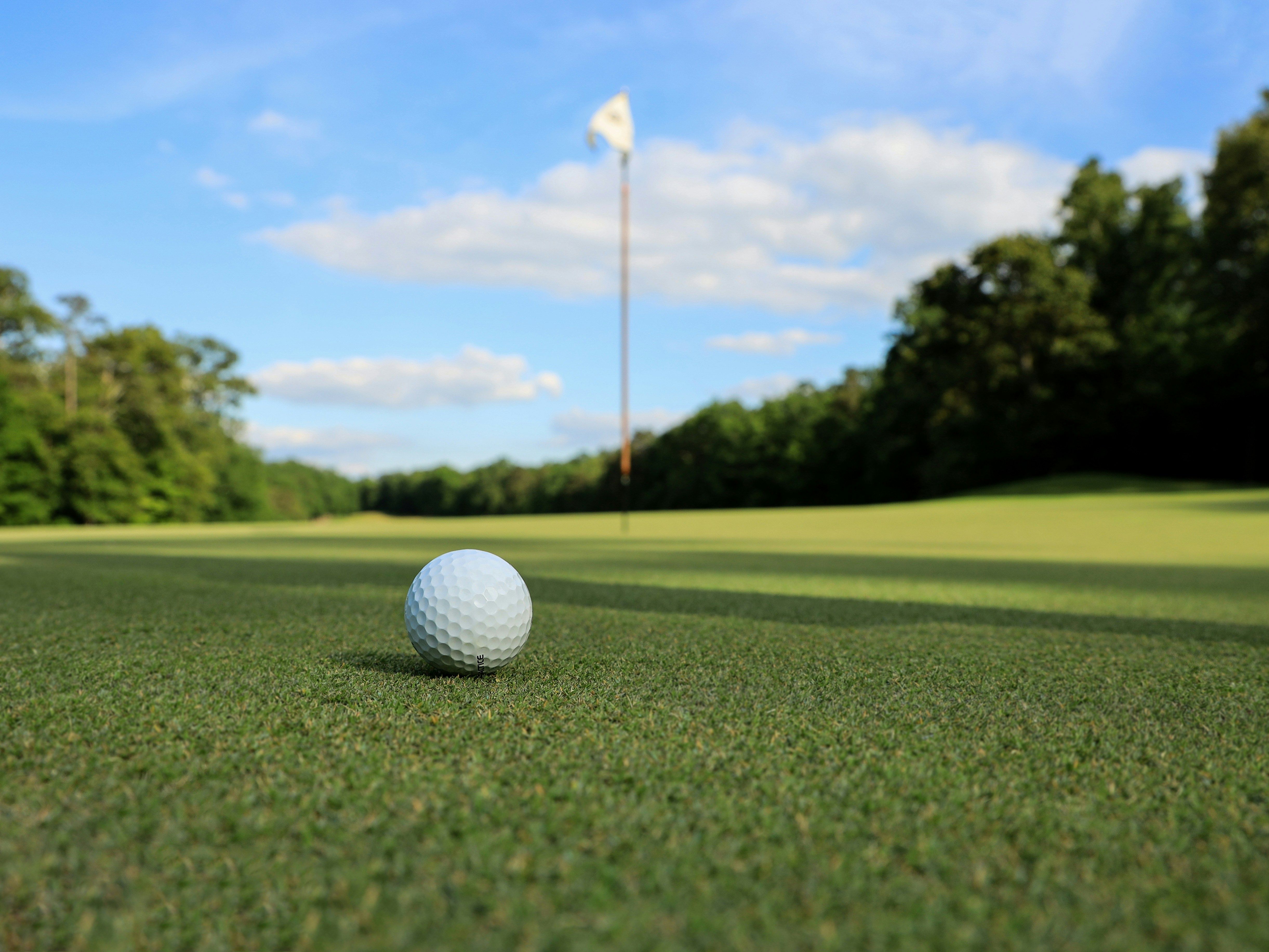 Golf ball on a putting green with flagstick in the distance under a blue sky