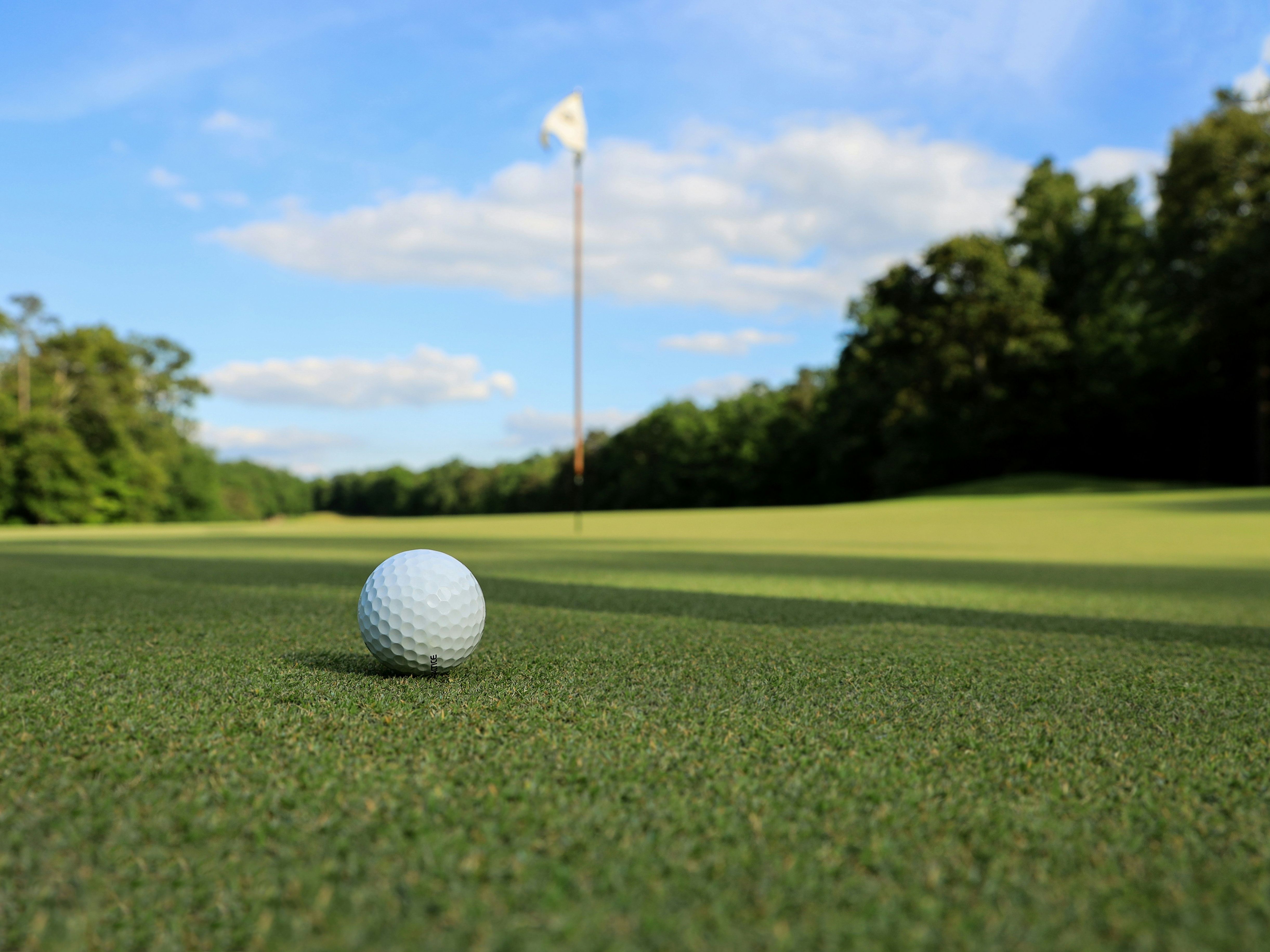 Golf ball on a putting green with flagstick in the distance under a blue sky