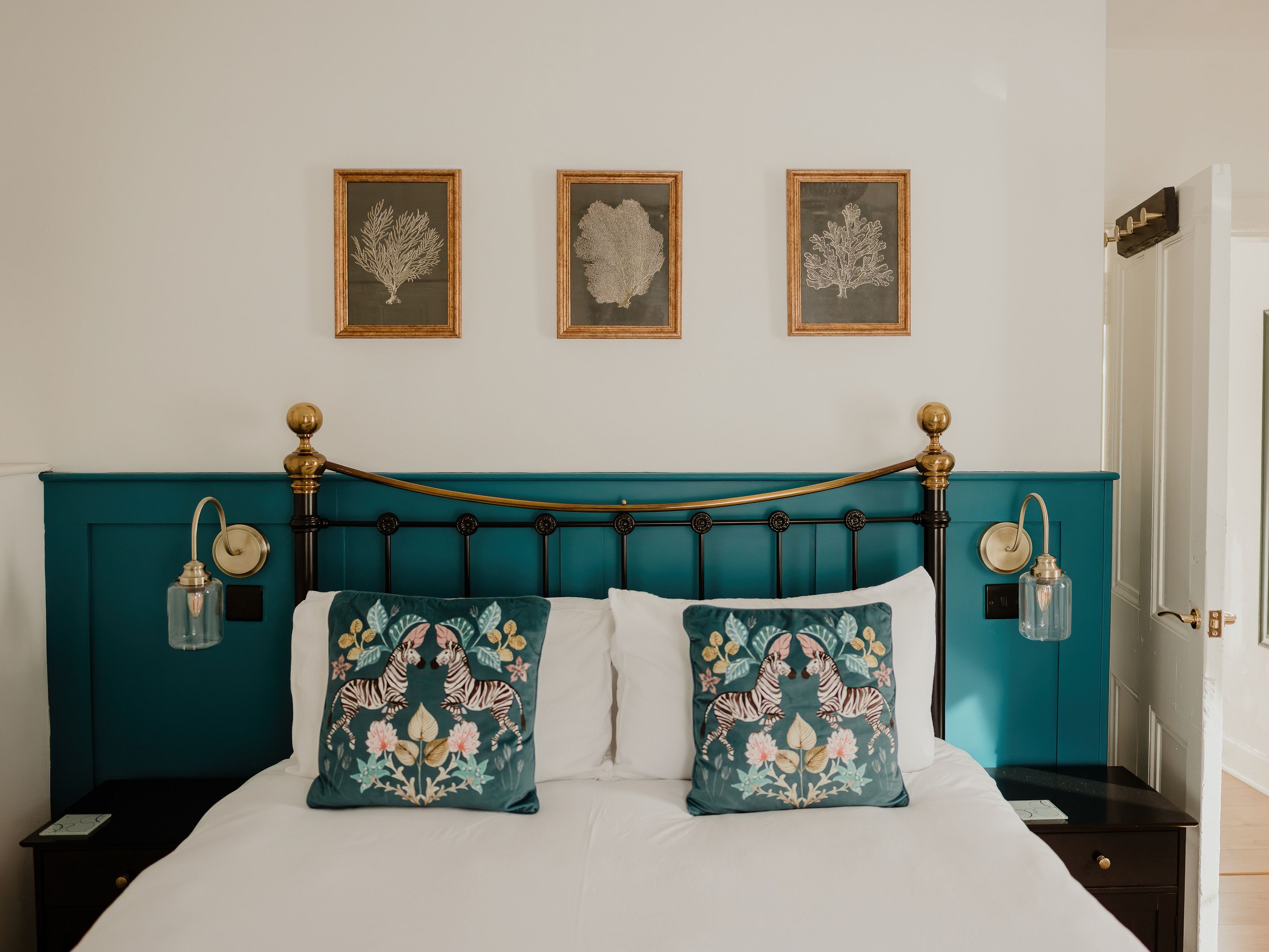 Stylish bedroom with teal panelled headboard, brass wall lights and zebra print cushions